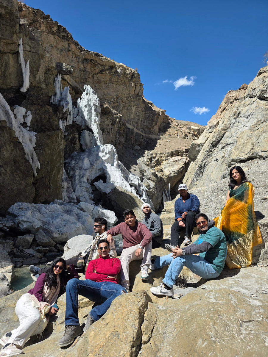 A group lounging on rocks below an icefall under a blue sky