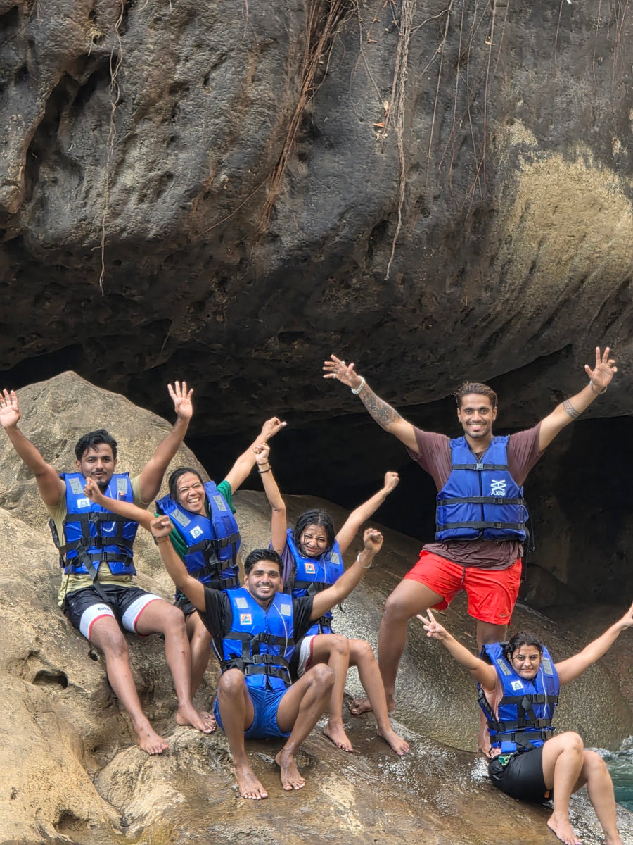 A group in life jackets with their arms in the air beside a river pool