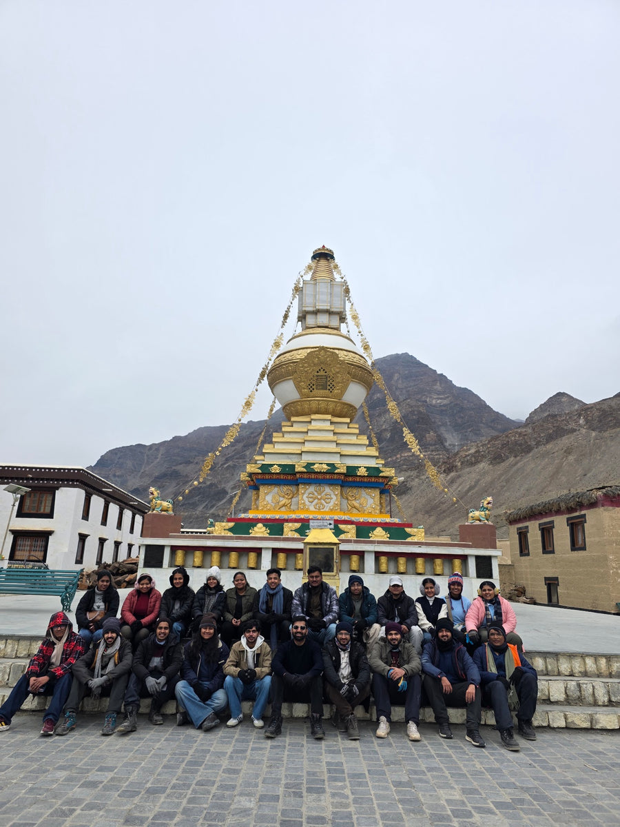A group seated on monastery steps below a golden stupa