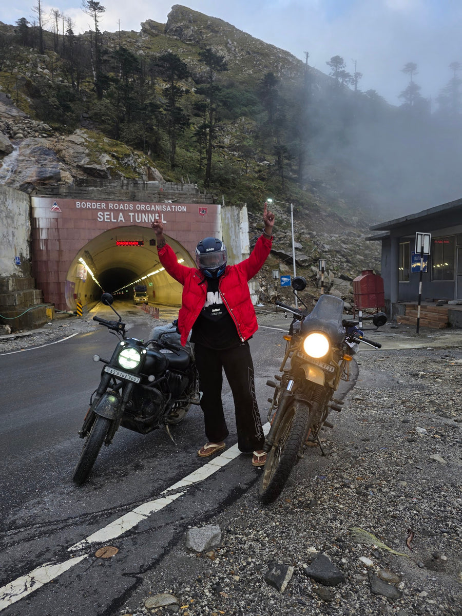 A rider with arms raised beside two motorbikes at the Sela Tunnel