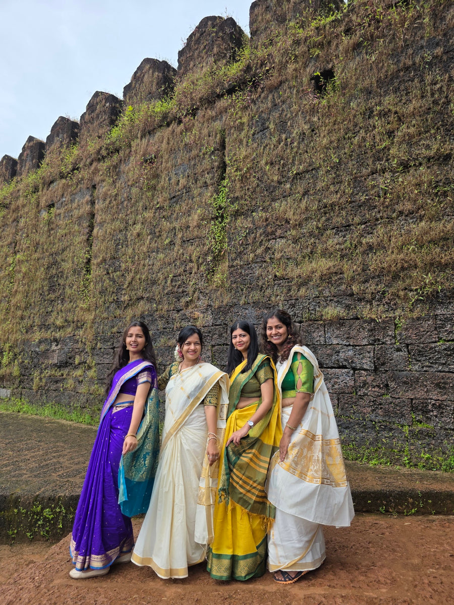 Four travellers in saris in front of an old stone fort wall