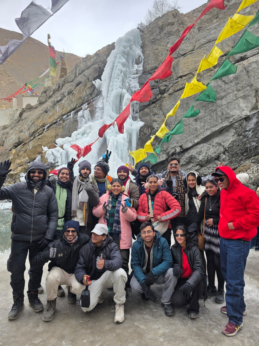 A group in front of a frozen waterfall strung with prayer flags