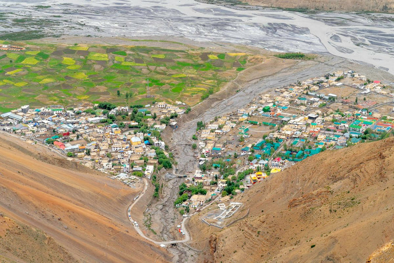 Kibber village and its green fields seen from above, with a dry river bed beside it
