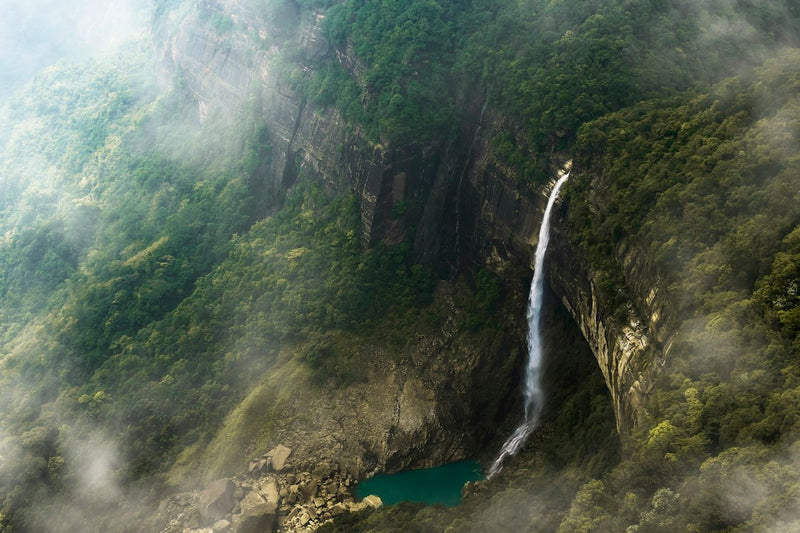 Nohkalikai Falls dropping from a forested cliff into a green pool