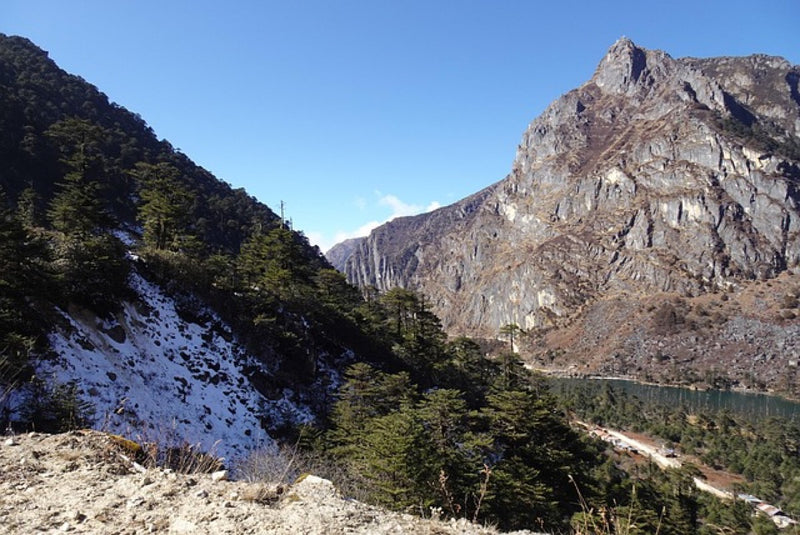 A high-altitude lake beside rocky mountains and conifer forest with patches of snow